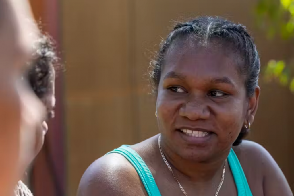 Young Aboriginal woman in light blue singlet talks to her friends